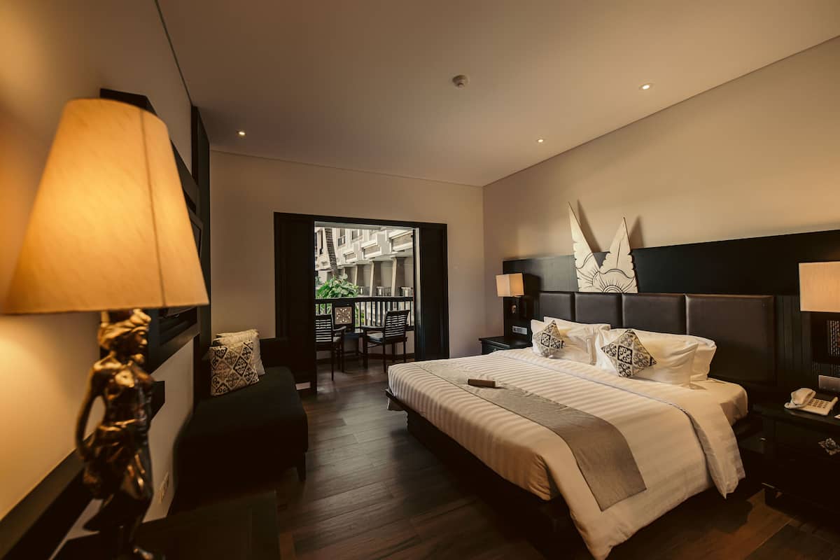 Habitación de hotel moderna con una cama grande, mesitas de noche, un escritorio y vistas a la ciudad a través de un ventanal.