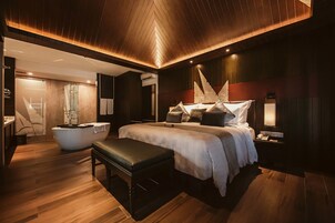 A modern bedroom with a large bed, a bench, a bathtub, and a vanity.
