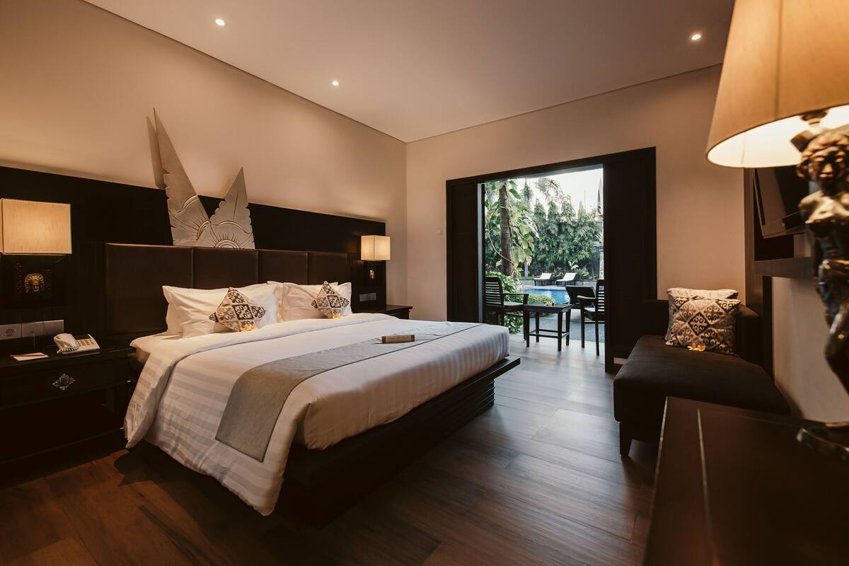 Un dormitorio de hotel moderno con una cama grande, lámparas de noche, una mesita de noche y vistas a un patio exterior.