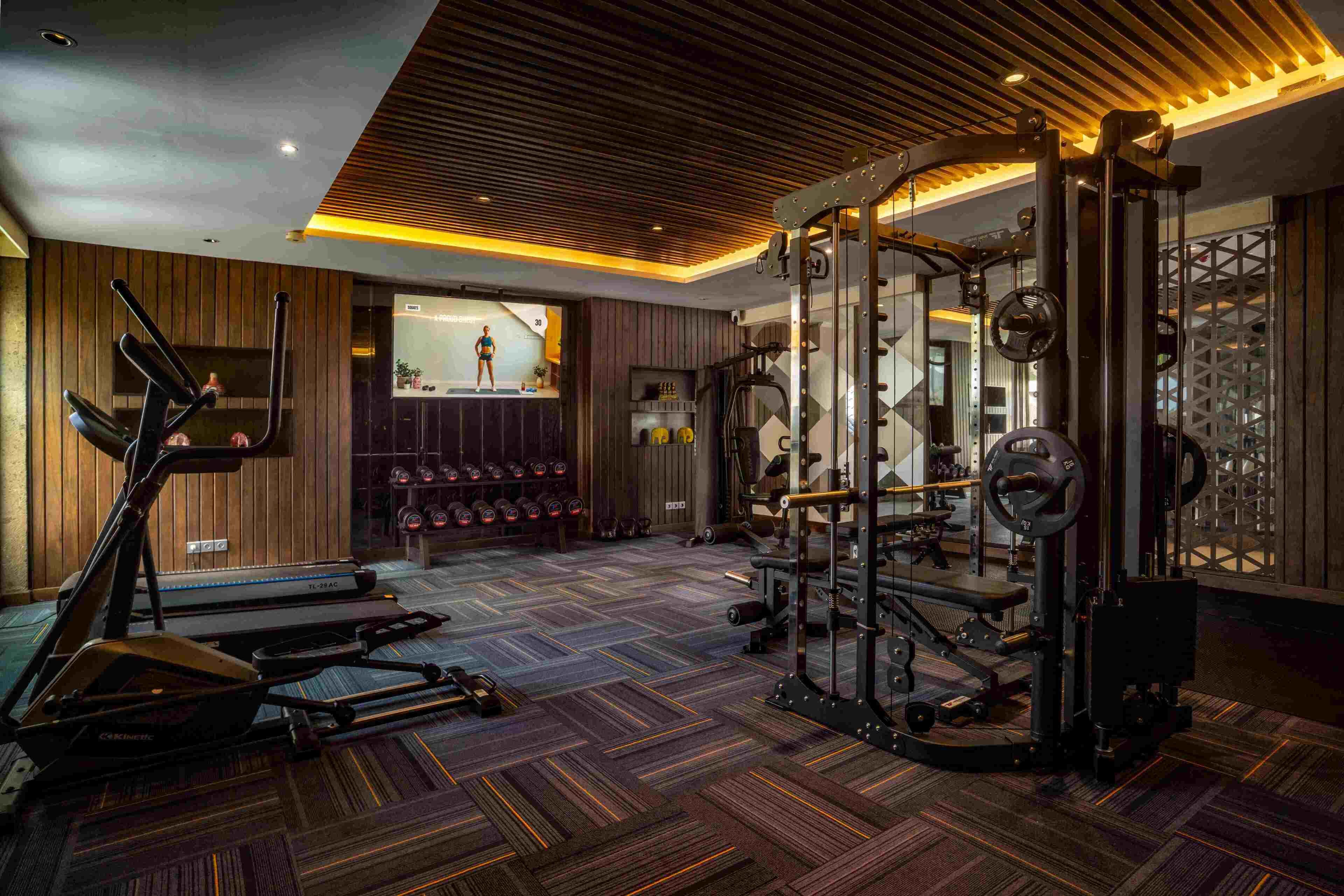 Une salle de sport équipée de tapis de course, d’un support pour les exercices de squat et de poids.