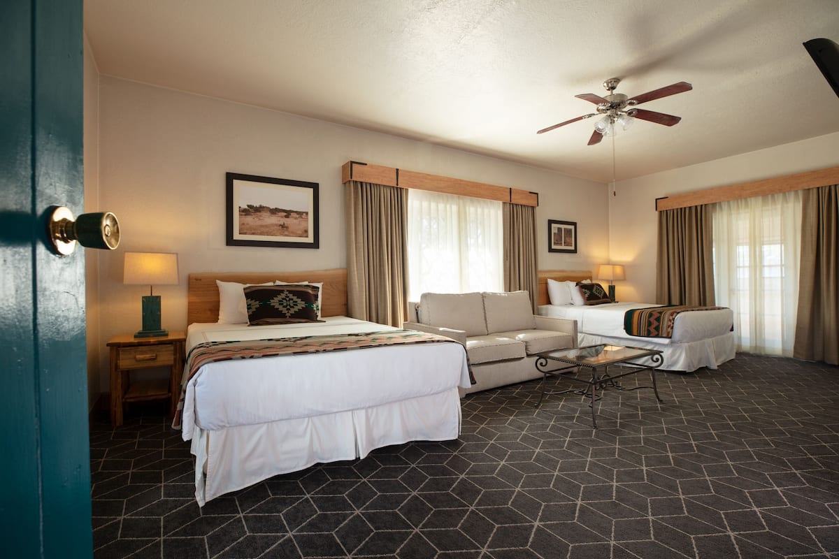 A hotel room with a bed, a sofa, a ceiling fan, and a window with curtains.