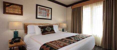 A hotel room with a large bed, two bedside lamps, a telephone, a framed picture on the wall, and a window with curtains.