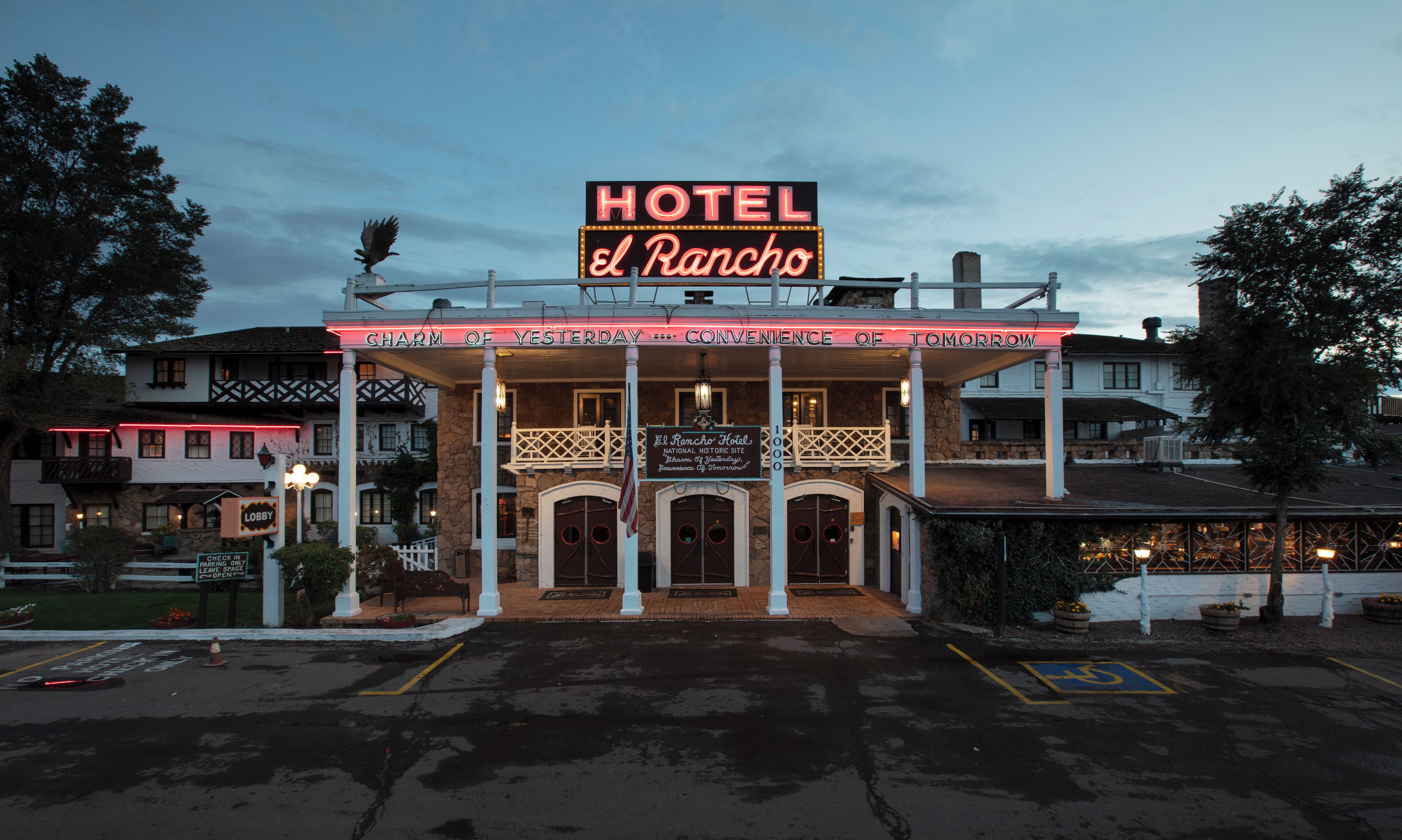 The exterior of the Hotel El Rancho, featuring a prominent neon sign, a balcony with railings, and a stone facade.