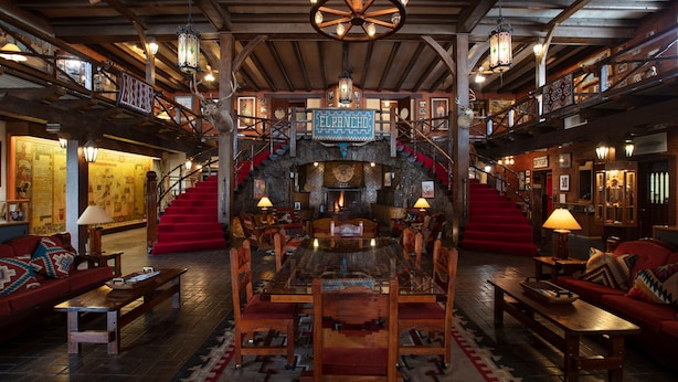 A spacious lobby with a central wooden coffee table surrounded by chairs, a staircase with red steps, and a sign reading "EL RANCHO". - Hotel El Rancho  (Gallup)