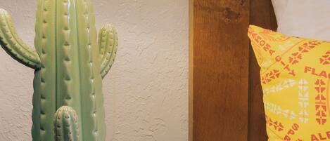 A cactus-shaped lamp on a table next to a bed with a patterned pillow.