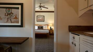A hotel room with a bed, a nightstand, a ceiling fan, and a kitchen area with cabinets.