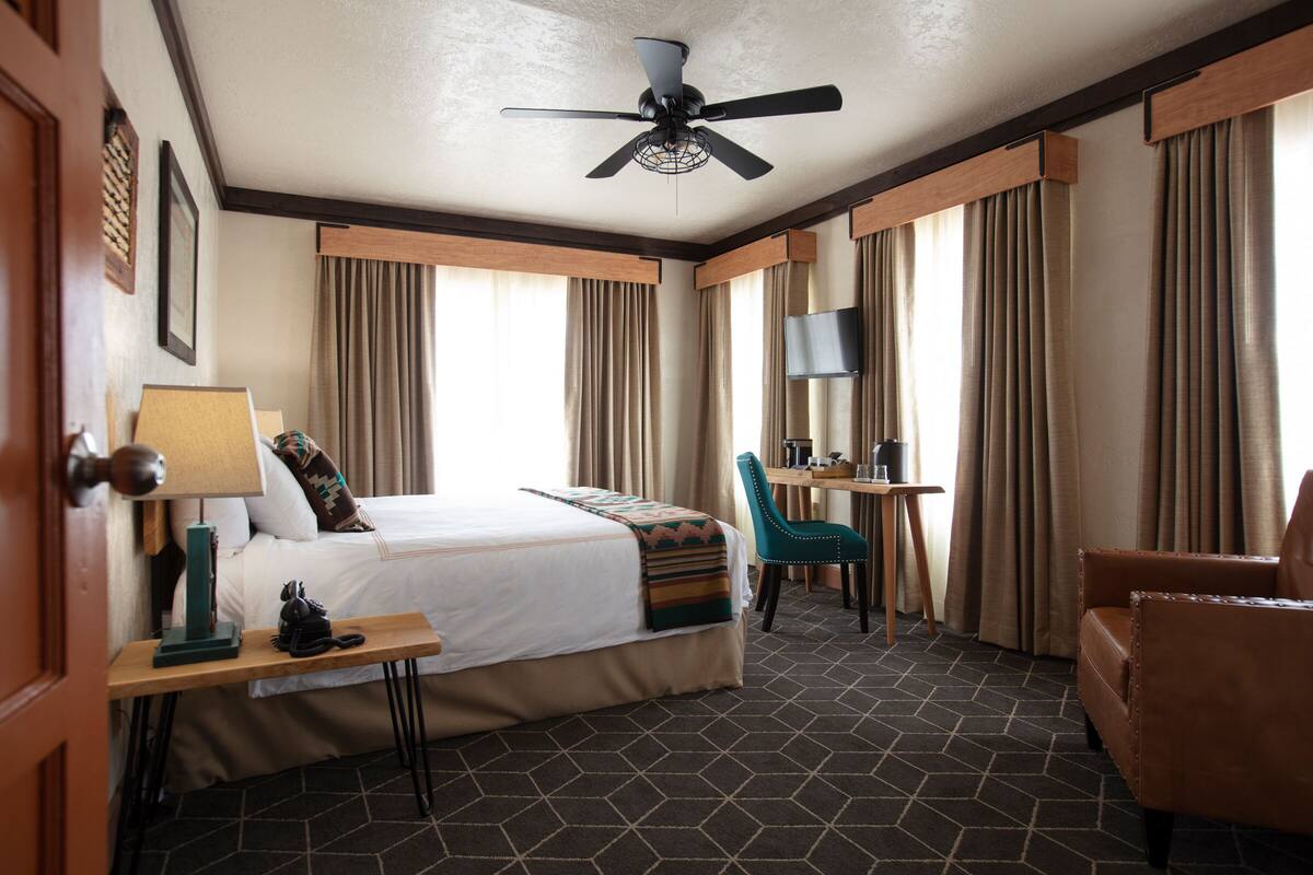 A hotel room with a bed, a desk, a chair, a television, and a ceiling fan.