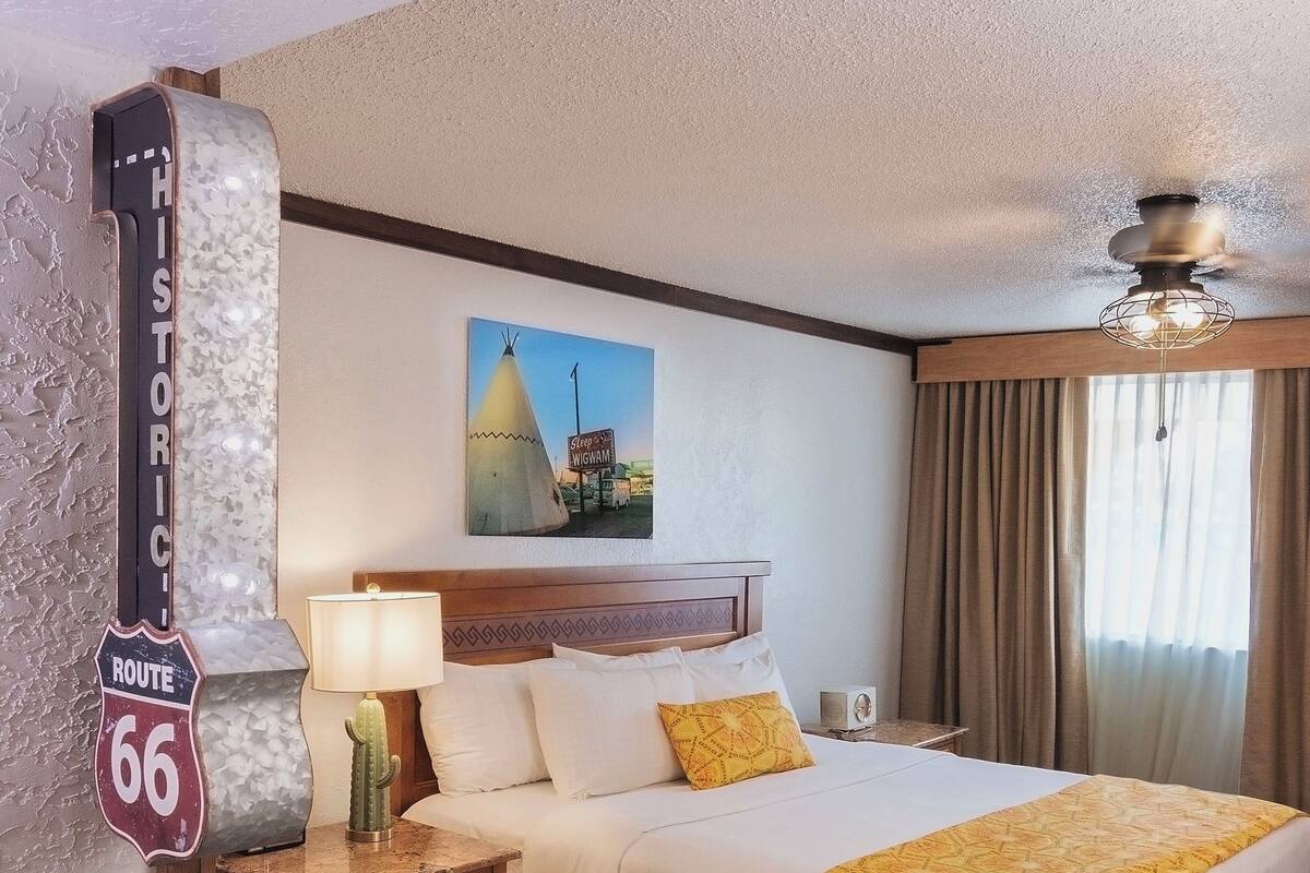 A hotel room with a large bed, a nightstand, a lamp, a chair, a painting of a teepee, and a sign reading "Historic Route 66".