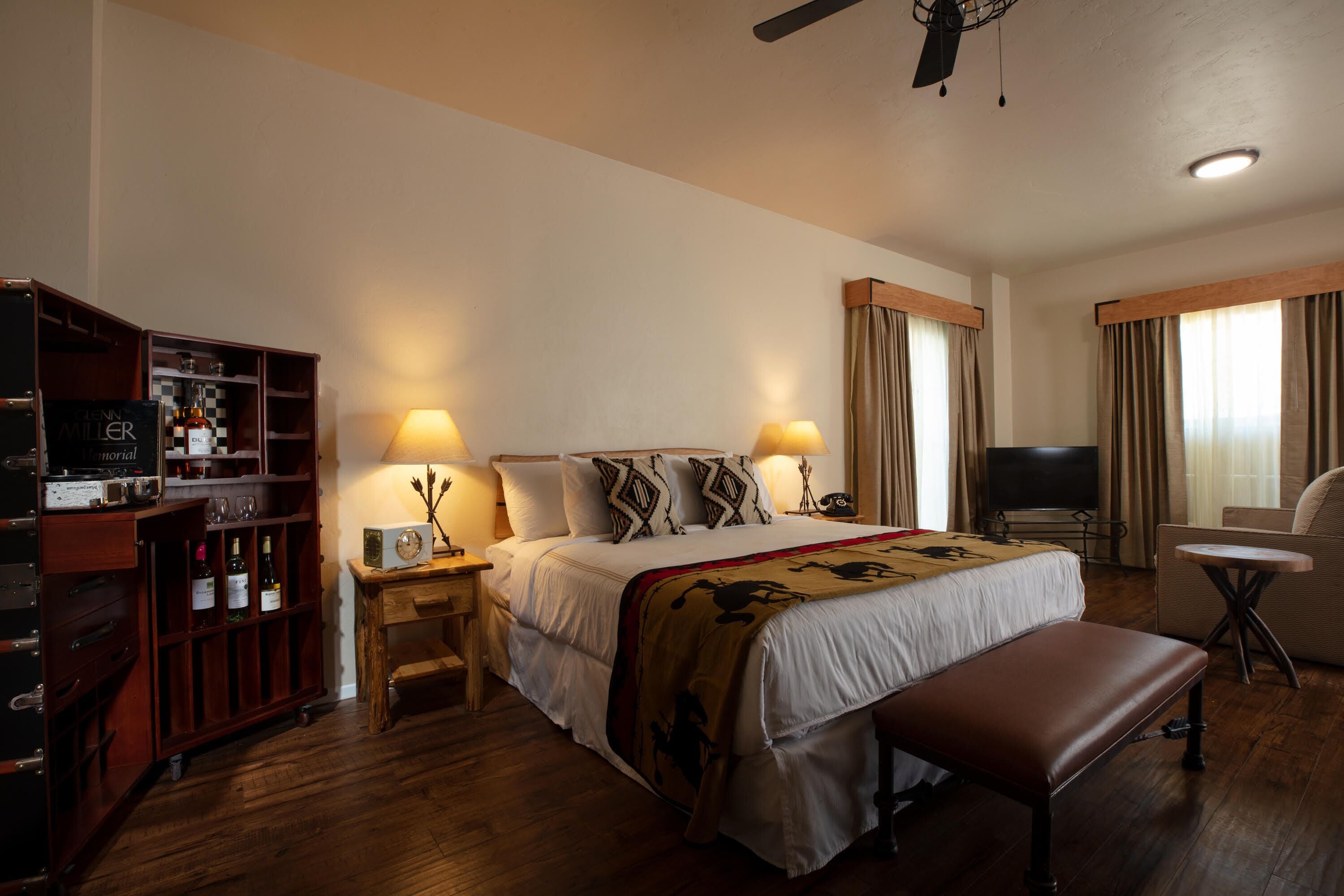 A hotel room with a bed, bedside lamps, a TV, a seating area, and a minibar.