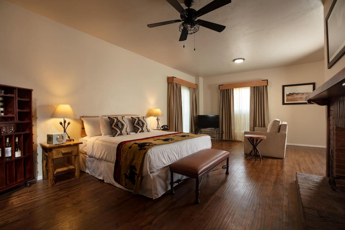 A hotel room with a large bed, a wooden bench, a small table, a bookshelf, and a television.