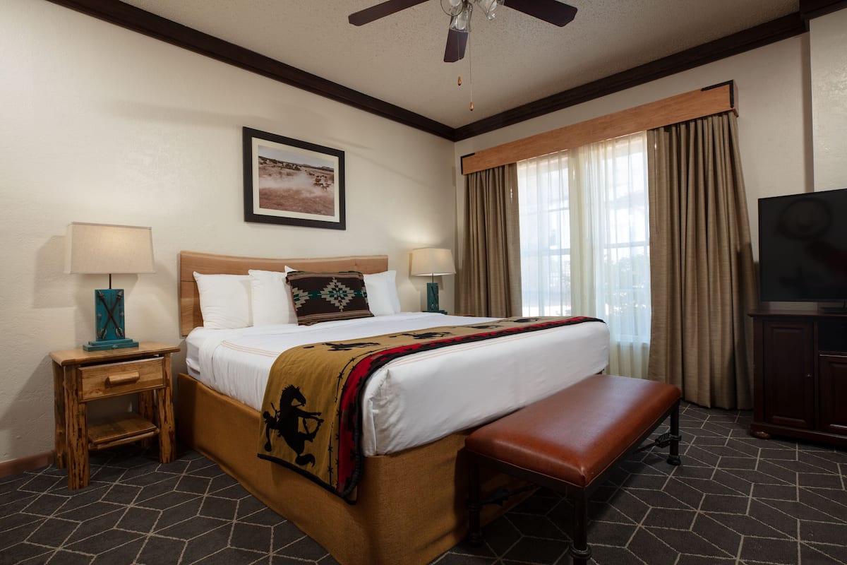 A hotel room with a bed, bedside tables, a bench, a television, and a window with curtains.