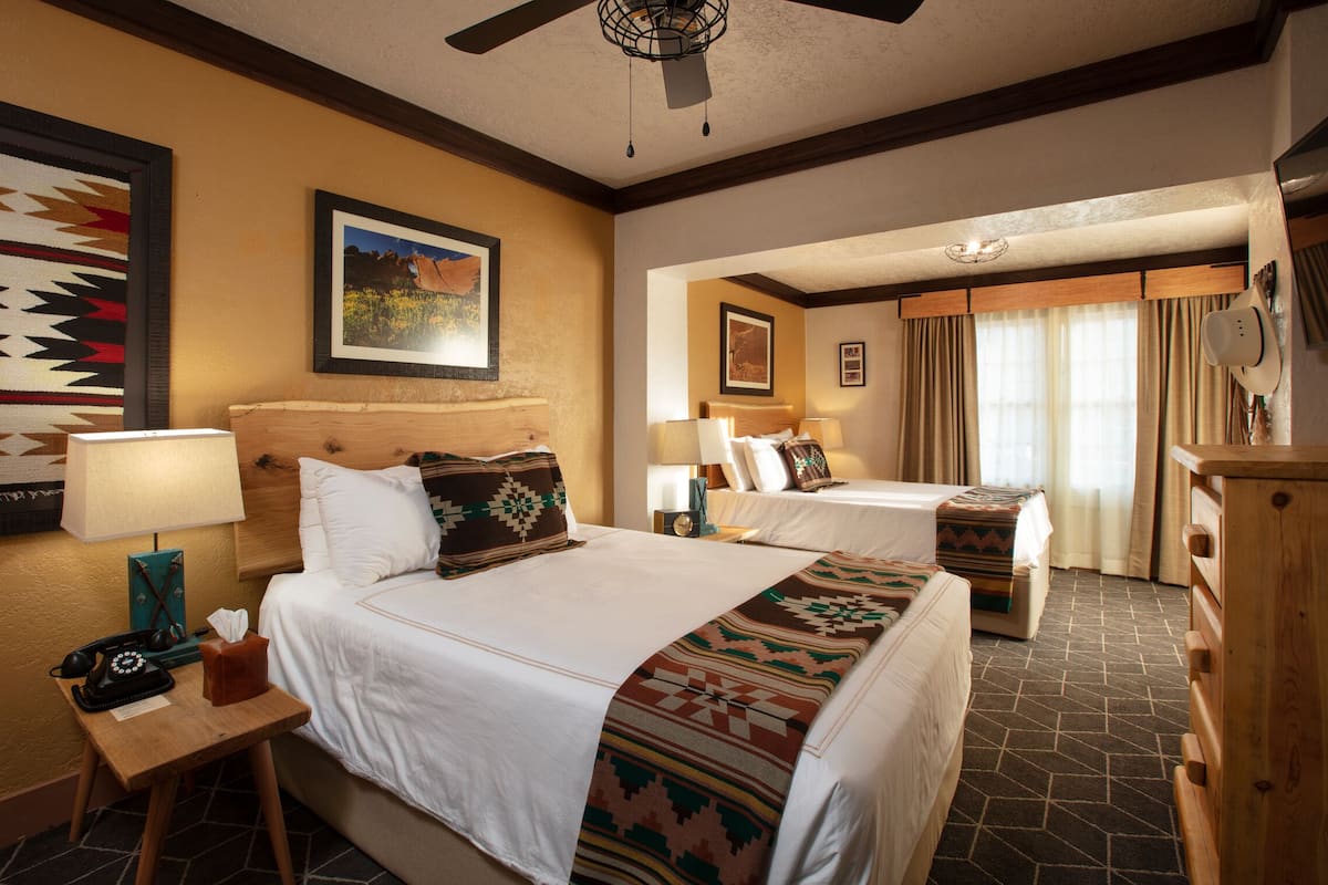 A hotel room with two beds, a wooden headboard, a telephone, a tissue box, and a wall-mounted picture.