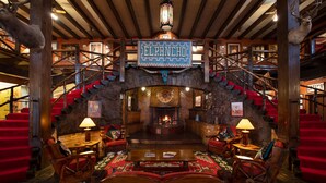 A lobby with a central fireplace, wooden furniture, and a staircase with red steps. - Hotel El Rancho  (Gallup)