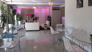A modern living room with a glass coffee table, white chairs, a white sofa, and a chandelier. There is a plant, a vase with flowers, and a sign that reads "HOLLYWOOD". - Hollywood VIP Hotel (Los Angeles)