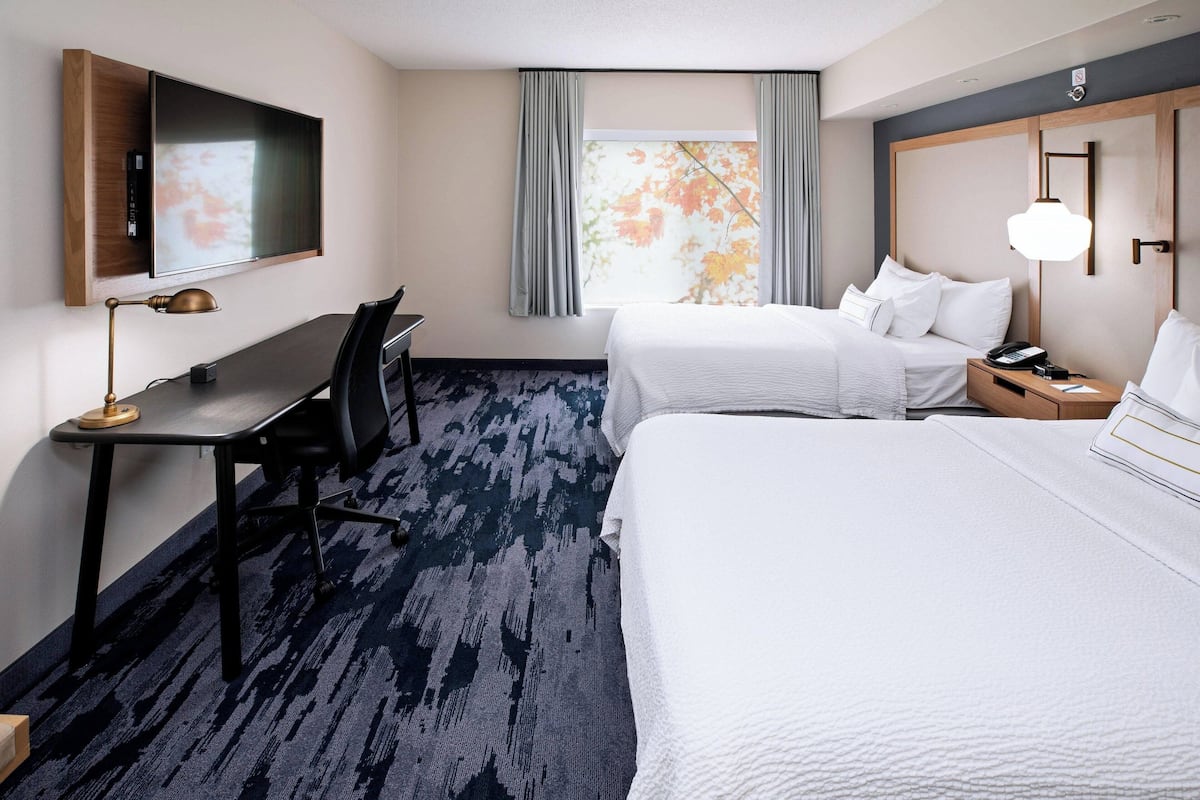 A hotel room with a large bed, a desk with a chair, a television mounted on the wall, and a window with curtains.