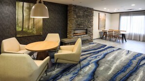 A modern living room with a stone fireplace, a round wooden table, and comfortable seating. - Fairfield Inn & Suites by Marriott Elizabethtown (Elizabethtown)