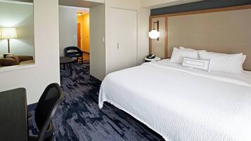 Habitación de hotel con una cama grande, un escritorio con silla, una lámpara y piso alfombrado.