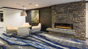 A modern living room with a stone fireplace, a blue abstract rug, and a dining area with two chairs and a table. - Fairfield Inn & Suites by Marriott Elizabethtown (Elizabethtown)