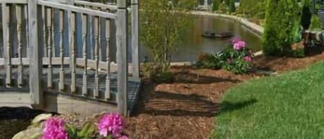 A garden with a wooden fence, a pond, and pink flowers.