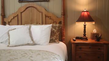 Una cama bien hecha con ropa de cama blanca y estampada, un cabecero de madera y una mesita de noche con una lámpara y un reloj.