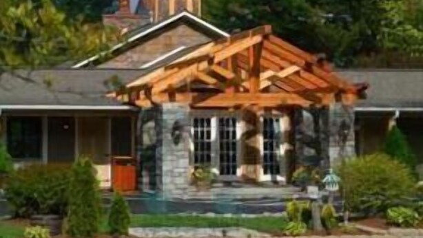 A lodge with a stone facade, a wooden porch, and a small tower with a weathervane. - The Village Inn (Blowing Rock)