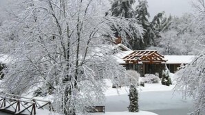 A traditional wooden building with a snow-covered roof, surrounded by snow-laden trees and a frozen pond. - The Village Inn (Blowing Rock)