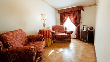 Una stanza con un divano decorato, una poltrona, un tavolino con una lampada, un armadio e una finestra con tende.