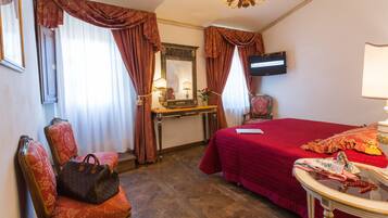 A hotel room with a bed, a chair with a handbag, a desk with a mirror, and a television on the wall.