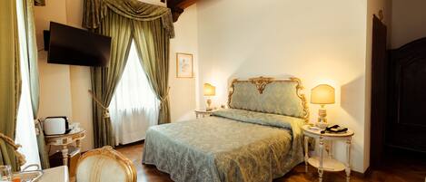 Un dormitorio con una cama, televisor montado en la pared, candelabro, mesita de noche con lámpara y una silla.