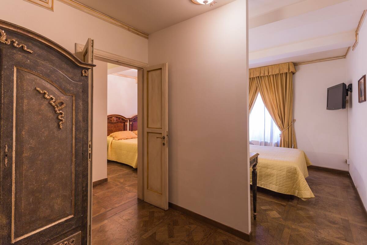 A hotel room with a wooden floor, a bed with a yellow bedspread, a wardrobe, and a television on the wall.
