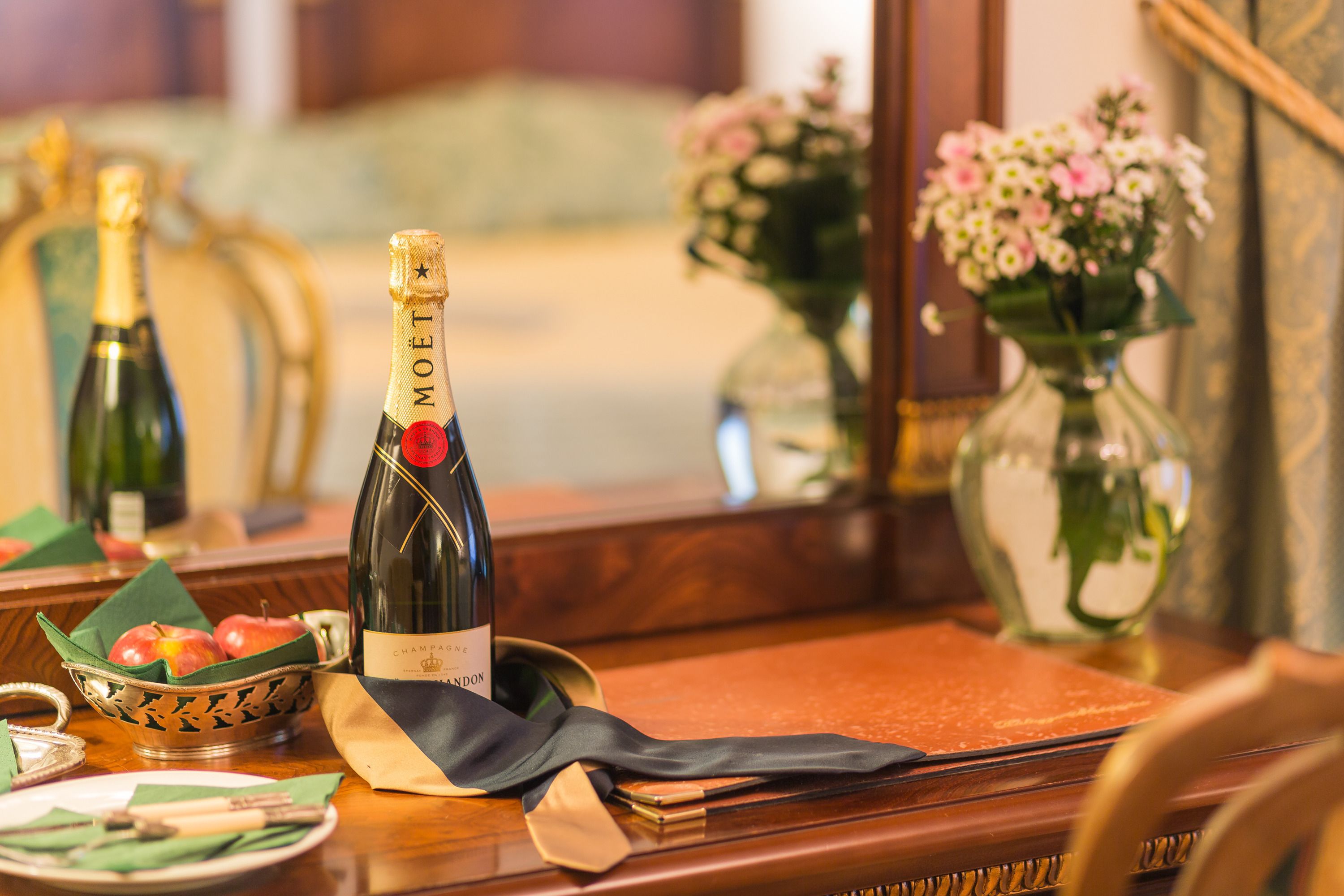A table with a bottle of Moët champagne, a folded napkin, and a small bowl of apples.