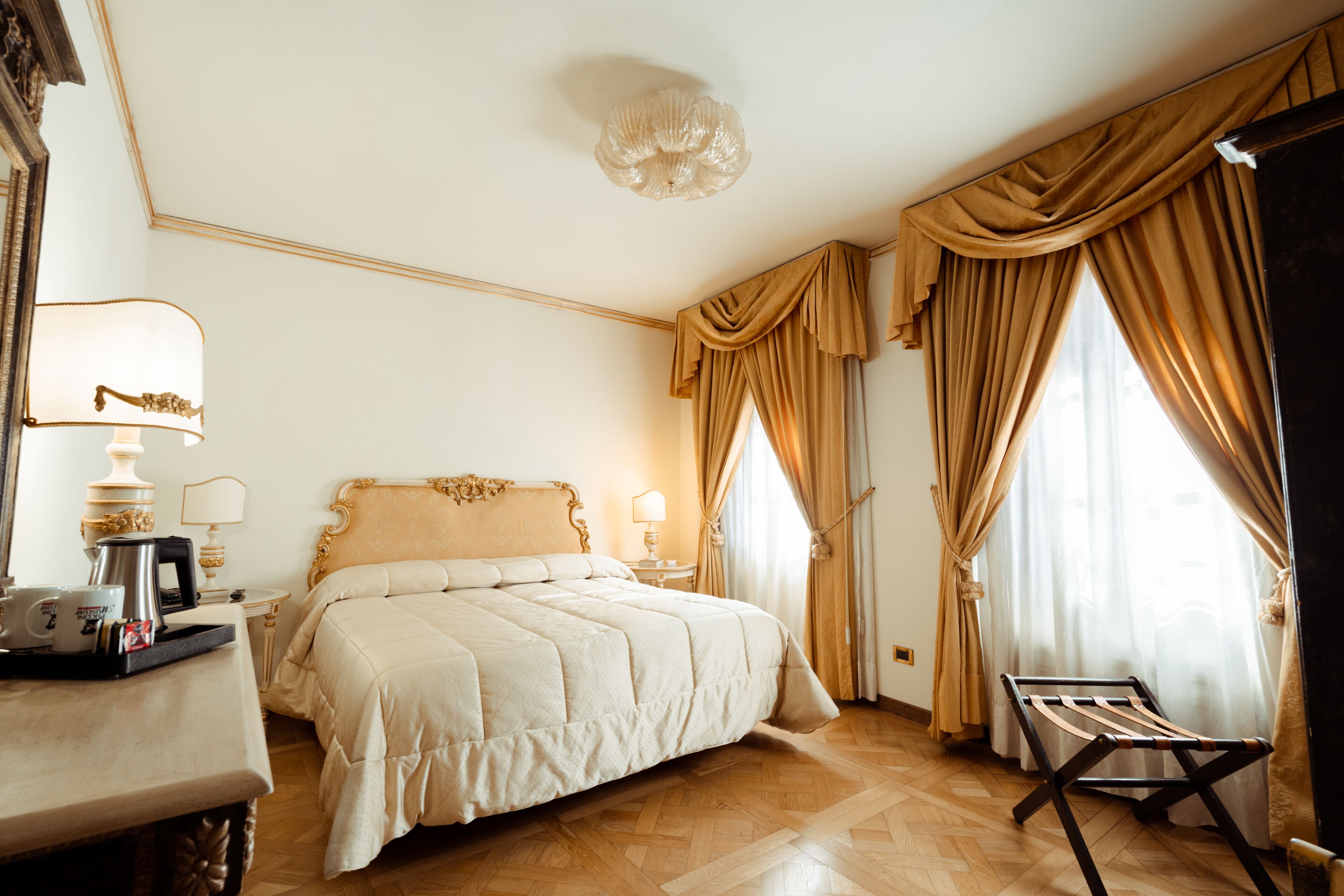 Habitación de hotel con una cama grande, un escritorio con lámpara, una cafetera y una ventana con cortinas.