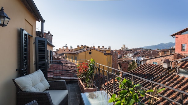 A rooftop terrace with wicker furniture and a glass table, overlooking a cityscape with terracotta roofs and a mountain in the distance. - Palazzo Alexander Hotel (Lucca)