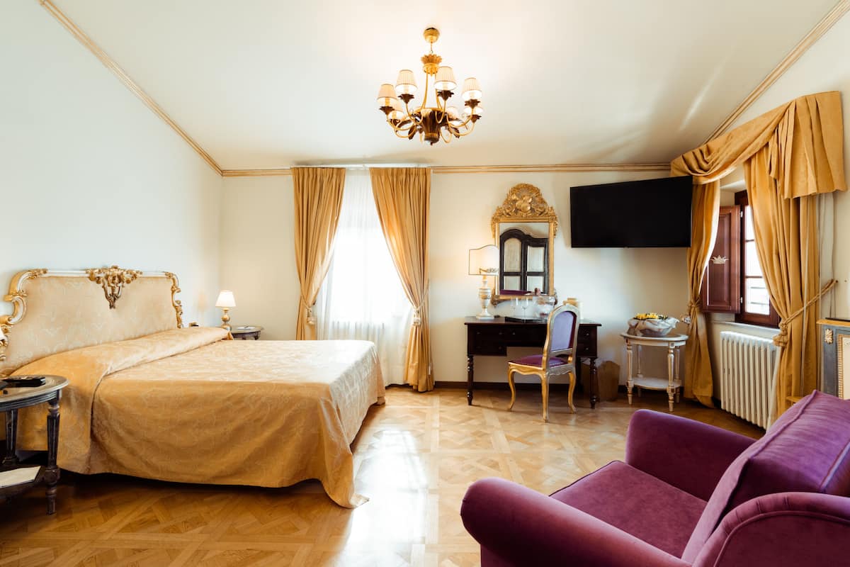 A hotel room with a large bed, a desk with a chair, a television, and a purple armchair.