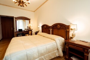 Camera d'albergo con un letto grande, una testiera in legno, una scrivania con una lampada, uno specchio e un armadio.