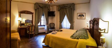 A hotel room with a large bed, a desk with a chair, a television, and a chandelier.