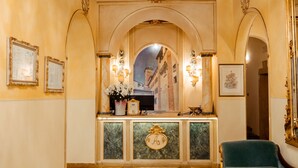 A reception area with a marble counter, framed artwork, and a green armchair. - Palazzo Alexander Hotel (Lucca)