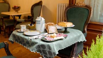 A dining table with a lace tablecloth, plates, a teapot, a cake, and a bag of snacks.