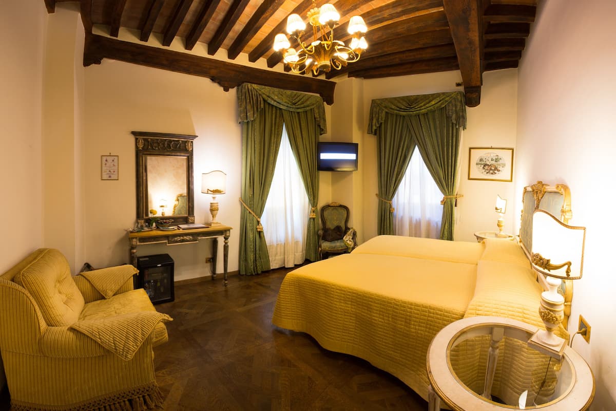 A hotel room with a bed, a chair, a desk, a television, and a chandelier.