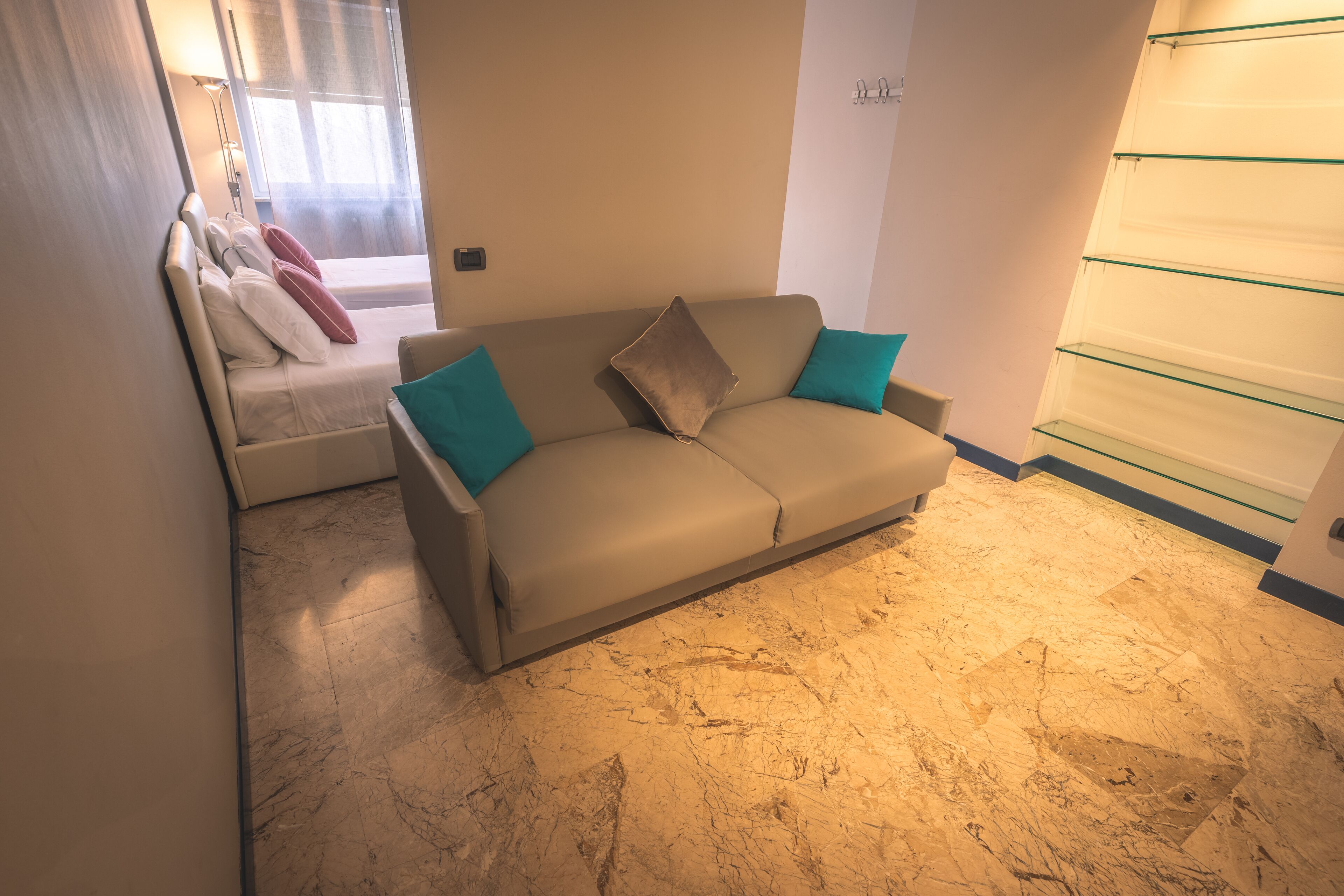 A modern living room with a beige sofa, teal cushions, a small table, and a glass shelf unit.
