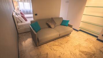 A modern living room with a beige sofa, teal cushions, a small table, and a glass shelf unit.