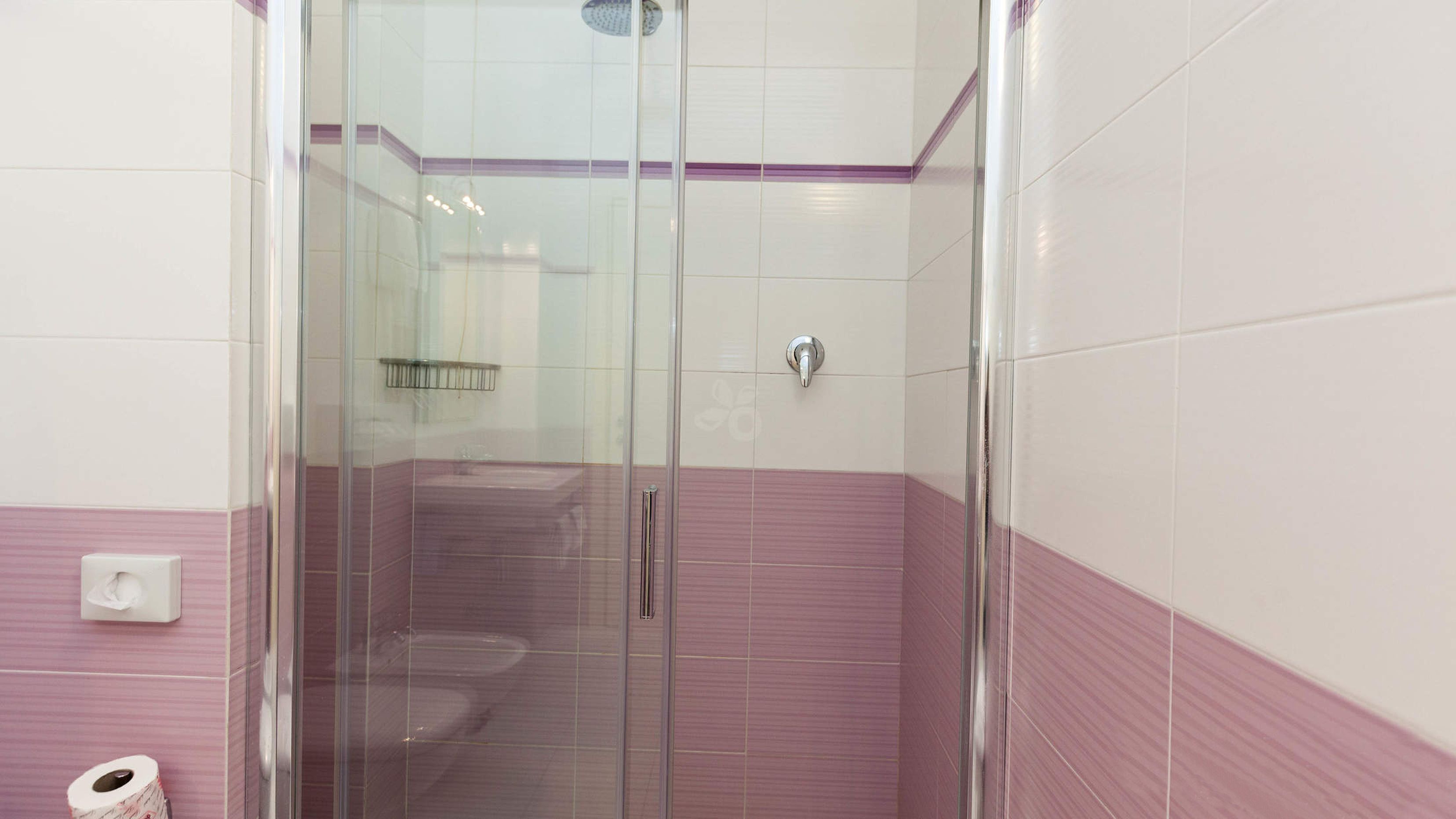 A bathroom with a glass shower enclosure, a toilet, and a paper towel dispenser.