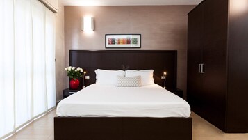 Un dormitorio moderno con una cama grande, una mesita de noche con un florero, una obra de arte enmarcada en la pared y un armario.