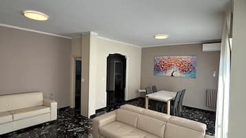 Una sala de estar moderna con un sofá color beige, una mesa de centro de vidrio y una zona de comedor con mesa y sillas.