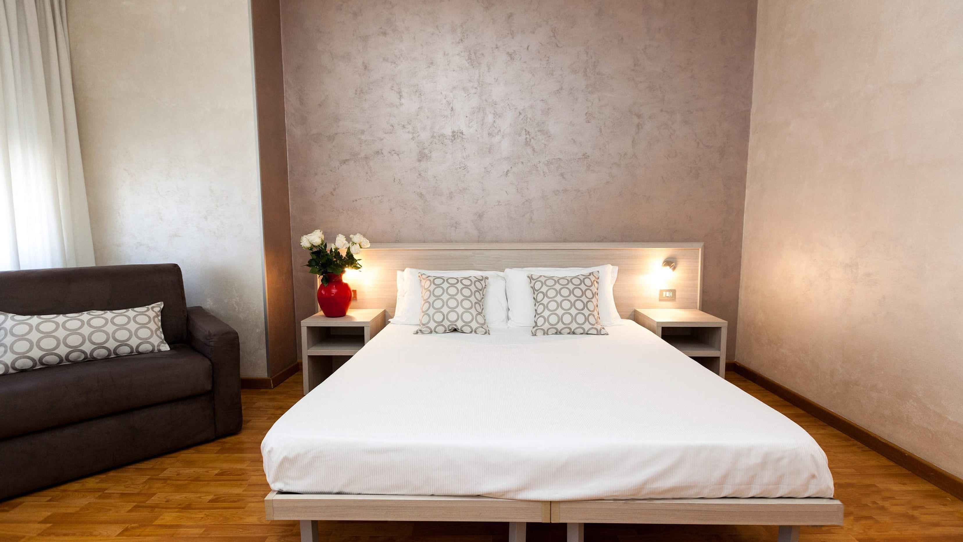 Un dormitorio ordenado con una cama grande, dos mesitas de noche, un sofá y un jarrón con flores.