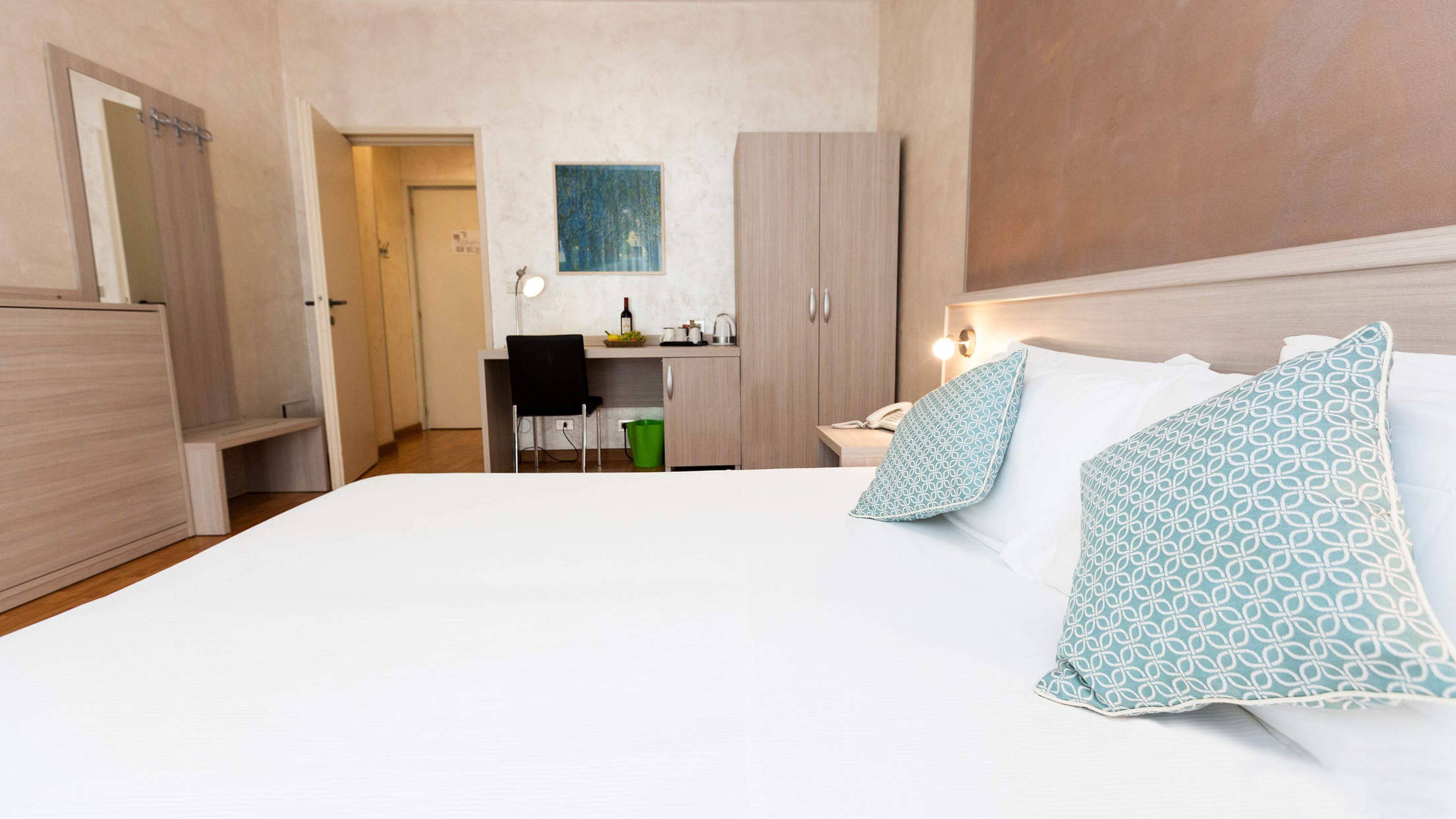 Habitación de hotel con una cama grande, dos mesitas de noche, un escritorio con silla y una zona de kitchenette.