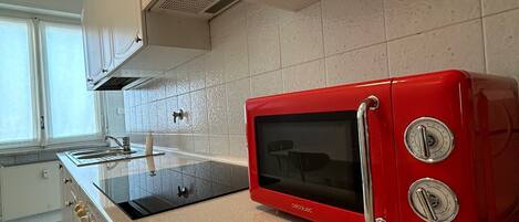 Une cuisine avec des meubles blancs, un micro-ondes rouge et une cuisinière noire.