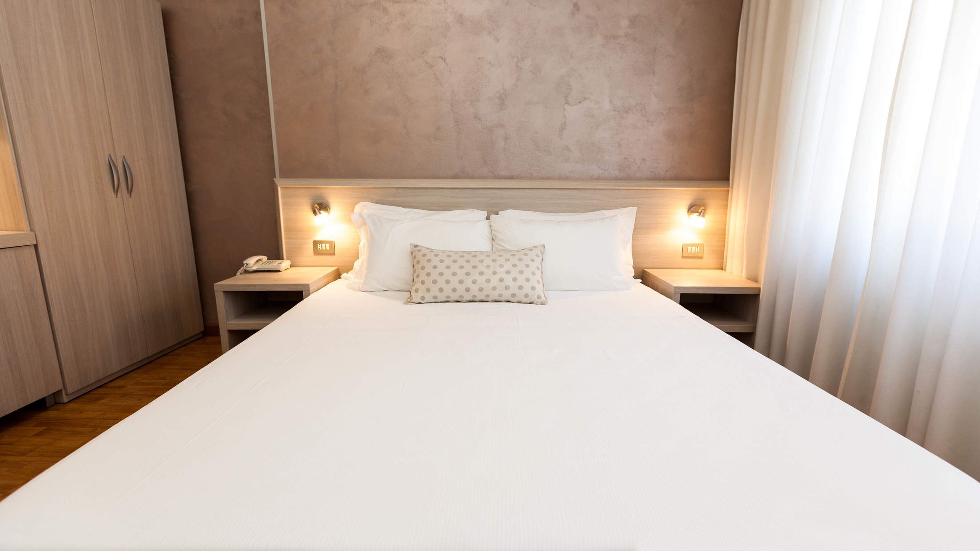 Una camera d'albergo con un letto grande, due comodini con lampade, un telefono e un armadio.