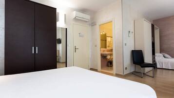 A bedroom with a large bed, a wardrobe, a chair, and a bathroom visible through an open door.