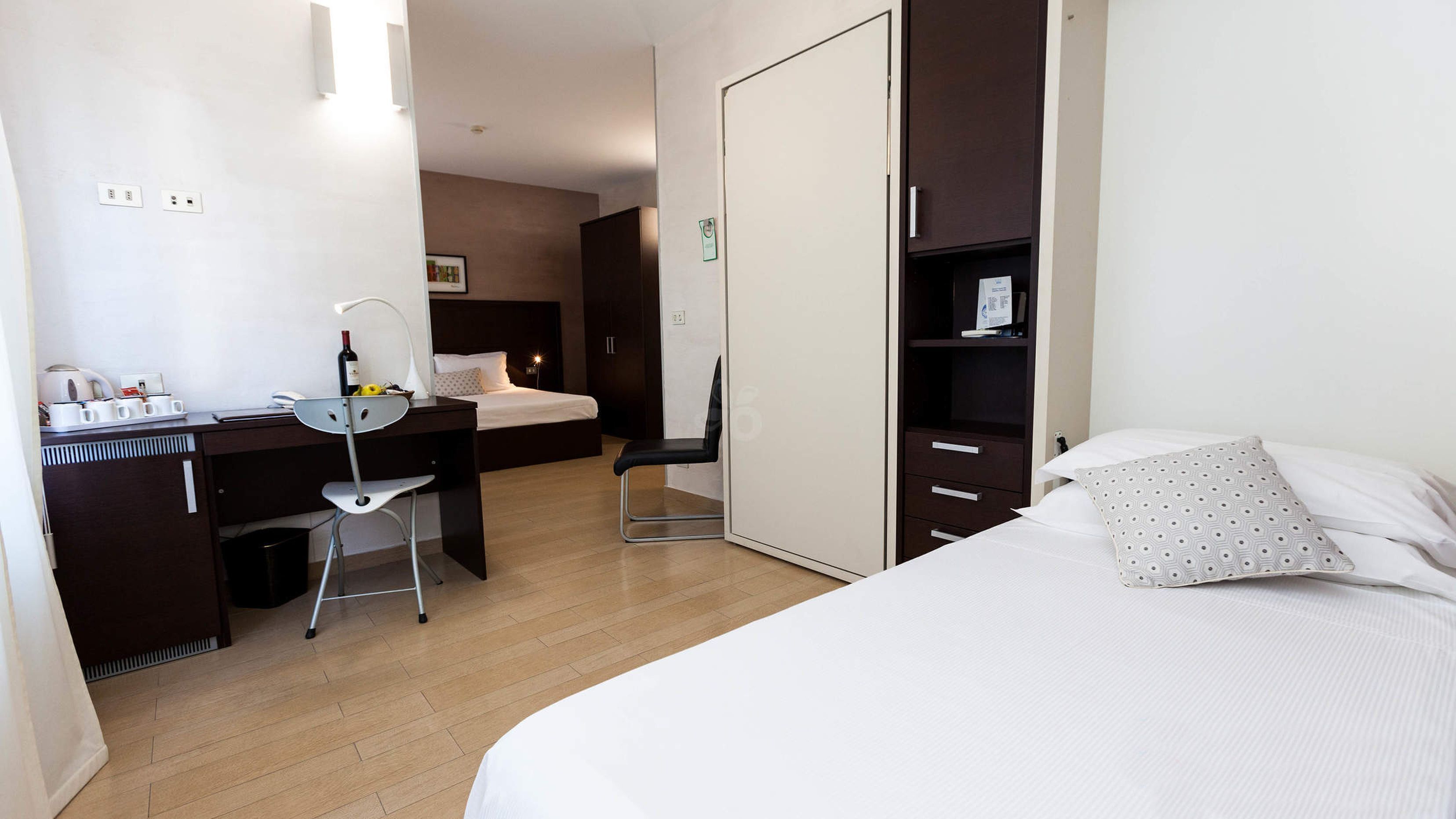 A hotel room with a bed, a desk with a chair, a wardrobe, and a bedside table.